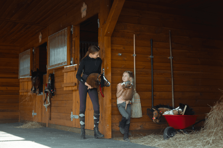 Mladi s Hobby Horse konji pred lesenimi hlevi konjeniškega kluba