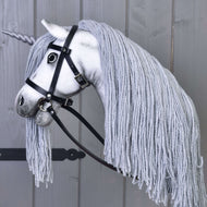 Pogled od strani na Hobby Horse samoroga Silver v črni uzdi z vajetmi, dolga siva griva iz preje mu pada čez vrat