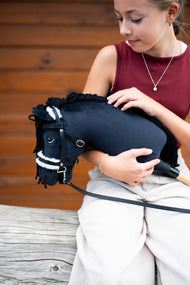 Deklica v bordo majici drži v naročju Hobby Horse konja Mahal s črno oglavko, tu s črno uzdo z belim krznom