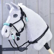 Siv Hobby Horse konj s črno vrvično oglavko z vozli in turkiznimi ovoji ter ujemajočimi se črnimi vajetmi čez vrat