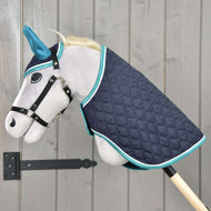 Svetlo siv Hobby Horse konj s črno oglavko nosi komplet Supreme Turquoise, temno modro prešito pregrinjalo s turkizno obrobo