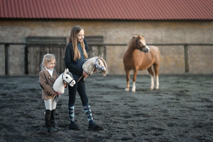 Dva otroka s Hobby Horse konji na zunanjem jahališču ob poniju