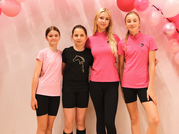 Štirje mladi udeleženci stojijo objeti pred nežno rožnatim ozadjem z rožnatimi baloni, v športnih rožnatih in črnih majicah s črnimi kratkimi hlačami ali pajkicami ter z logotipom Hobby Horse.