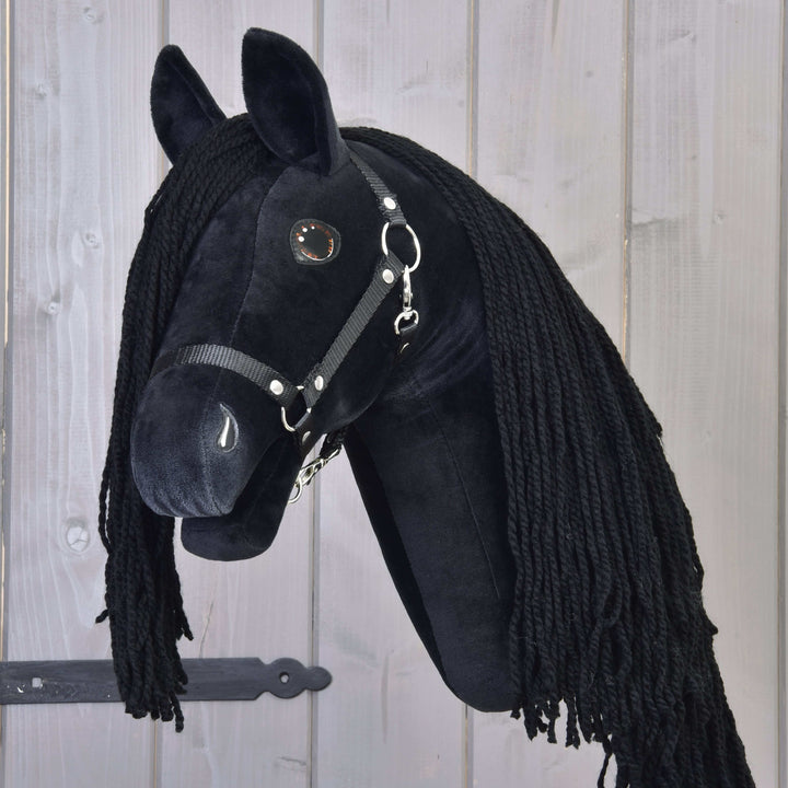 Črn Hobby Horse konj z dolgo črno grivo iz preje in uzdo na lesenem ozadju s temnim kovinskim tečajem.