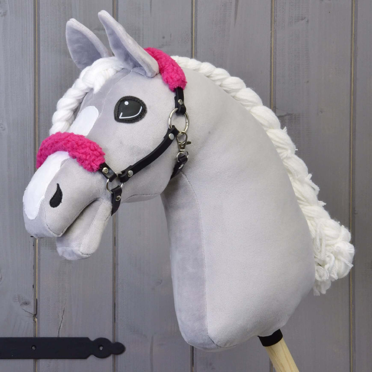 Siv plišast Hobby Horse konj z belo liso in spleteno grivo nosi črno oglavko s kodrastim živo roza krznom
