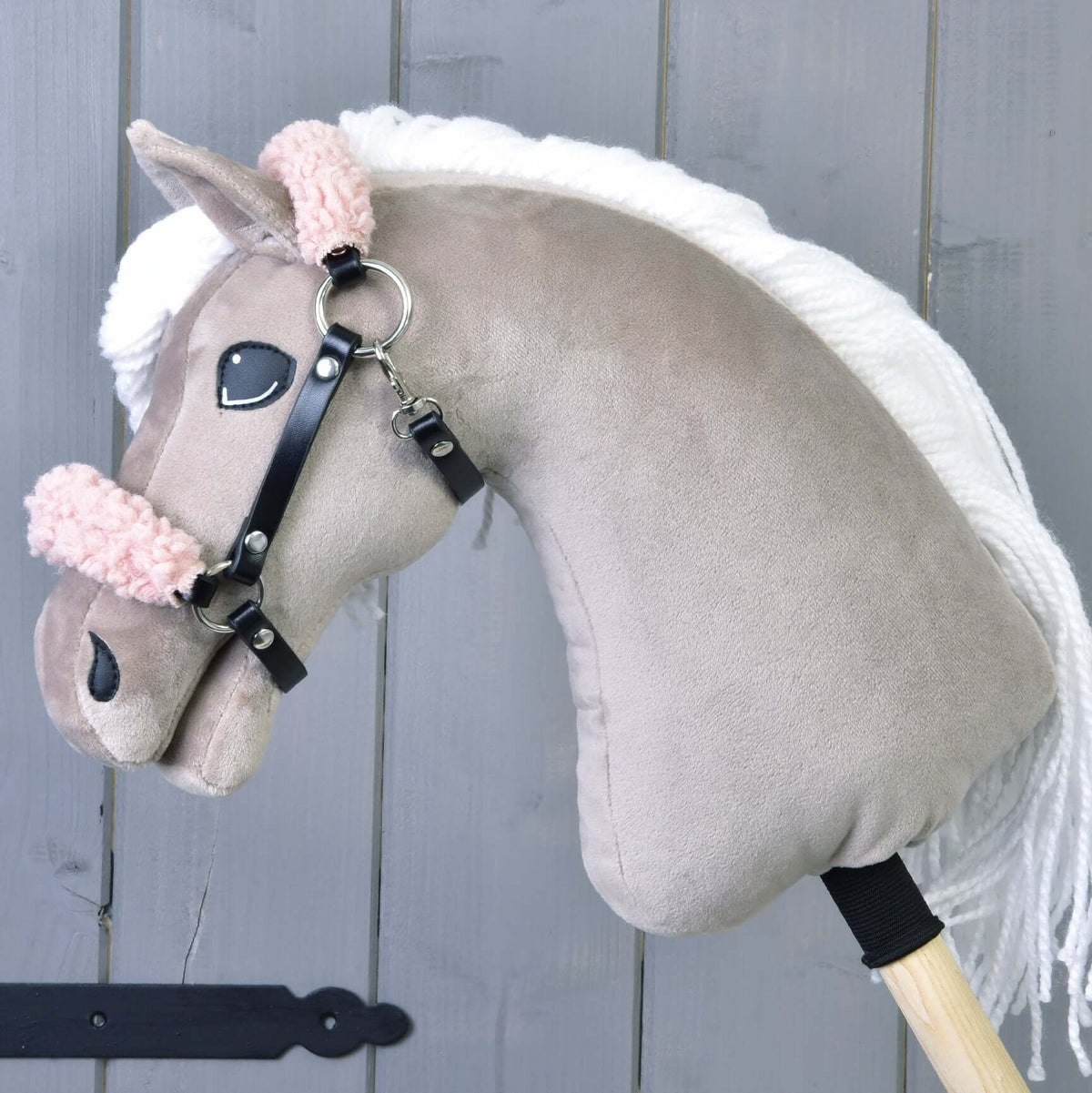 Bež plišast Hobby Horse konj z belo grivo nosi črno oglavko s kodrastim staro roza krznom na nosniku in zatilnem jermenu