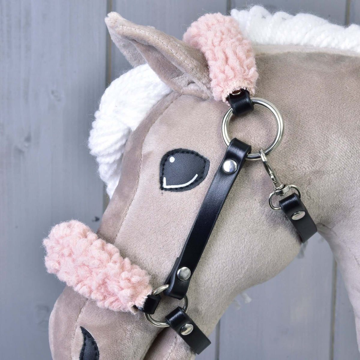 Bližnji posnetek črne oglavke iz umetnega usnja na bež Hobby Horse konju: kodrasto roza krzno, srebrn obroček in karabin