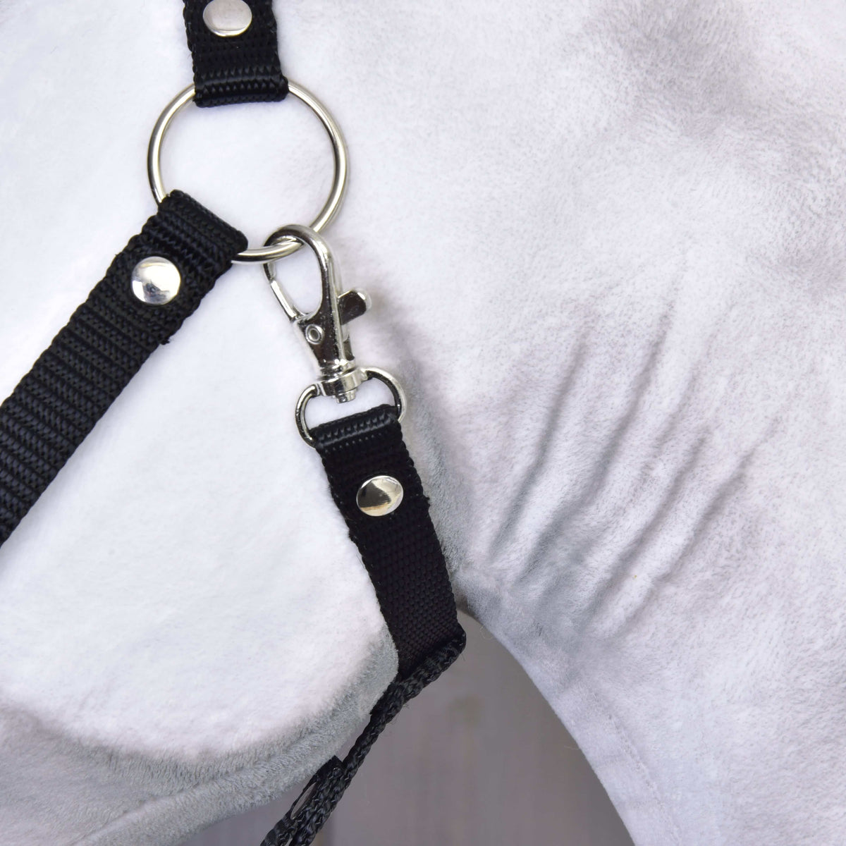 Bližnji posnetek srebrnega obročka in karabina črne oglavke na belem plišastem licu Hobby Horse konja Elektra