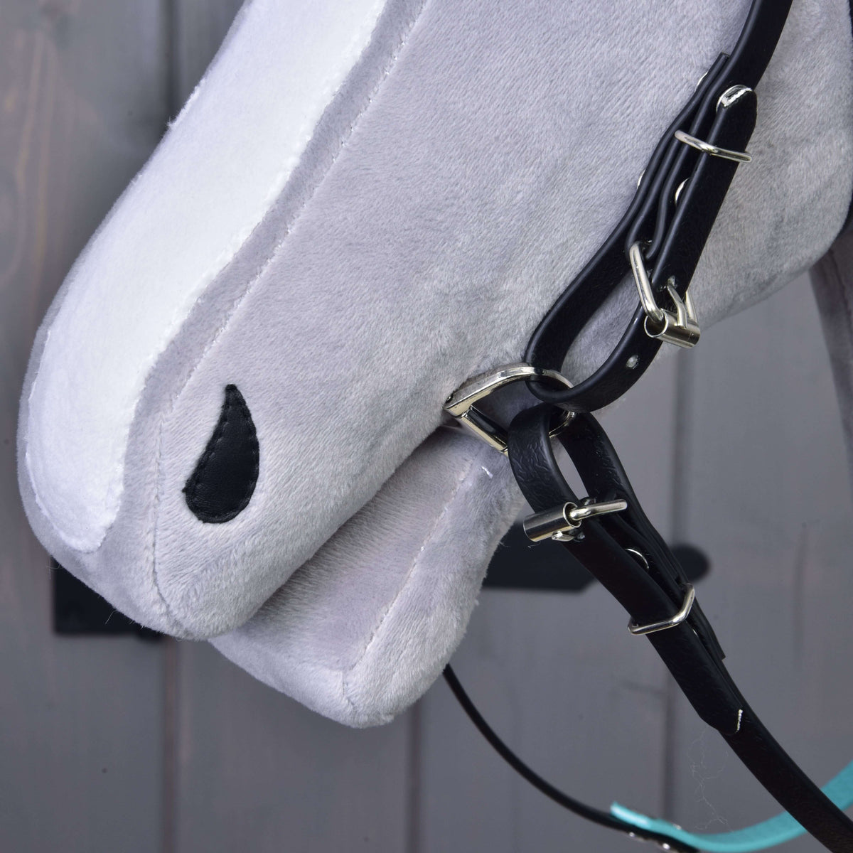 Bližnji posnetek gobca sivega Hobby Horse konja s črnimi ličnimi jermeni, zaponkami in obročkom brzde, brez nosnika