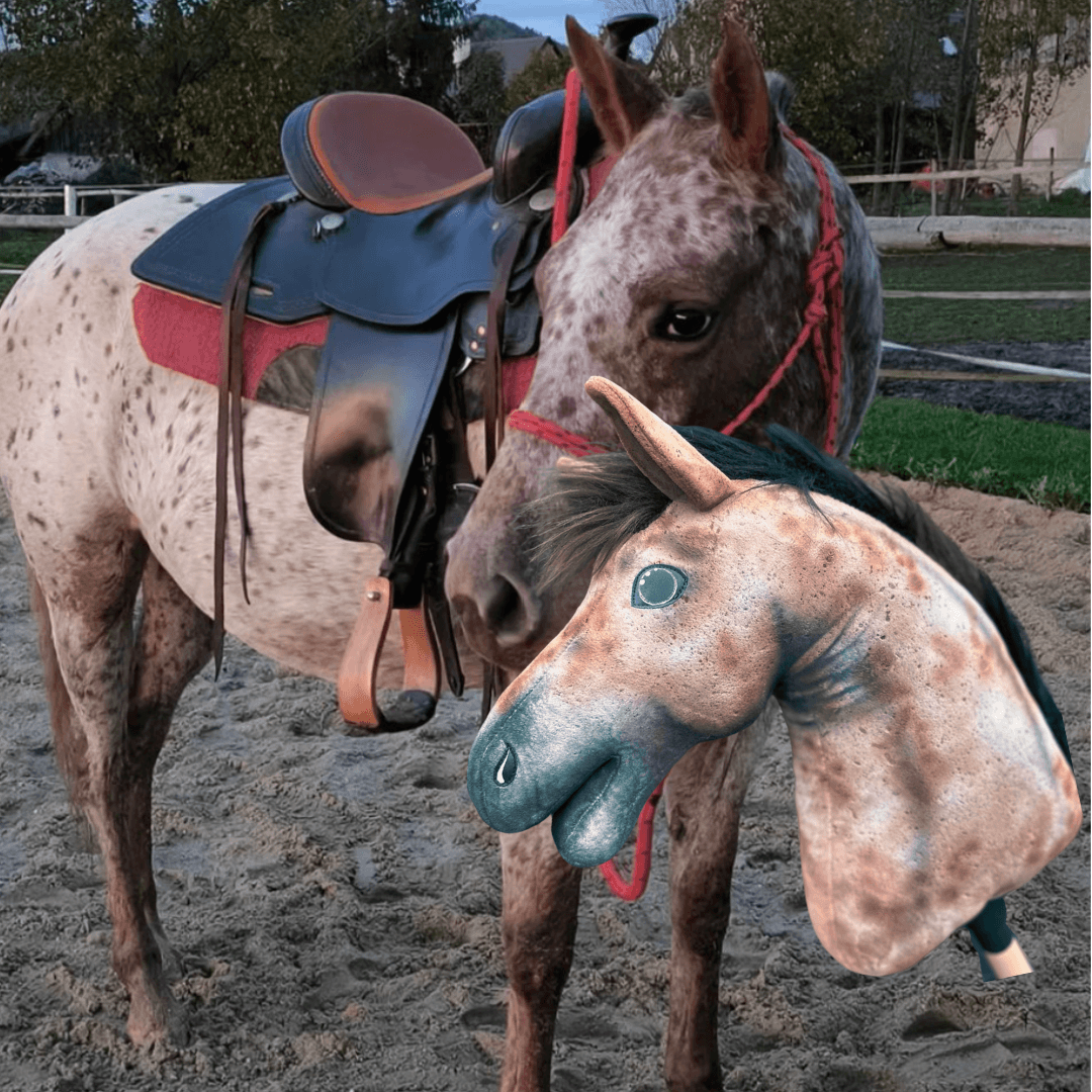 Spotted horse with a red rope halter on a sand arena behind its speckled Hobby Horse copy with a dark mane