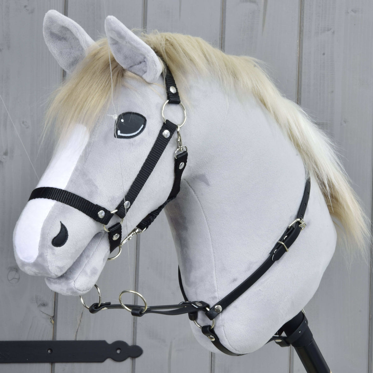 Svetlo siv Hobby Horse konj s črno oglavko nosi okoli vratu črn martingal z dvema srebrnima obročkoma spredaj