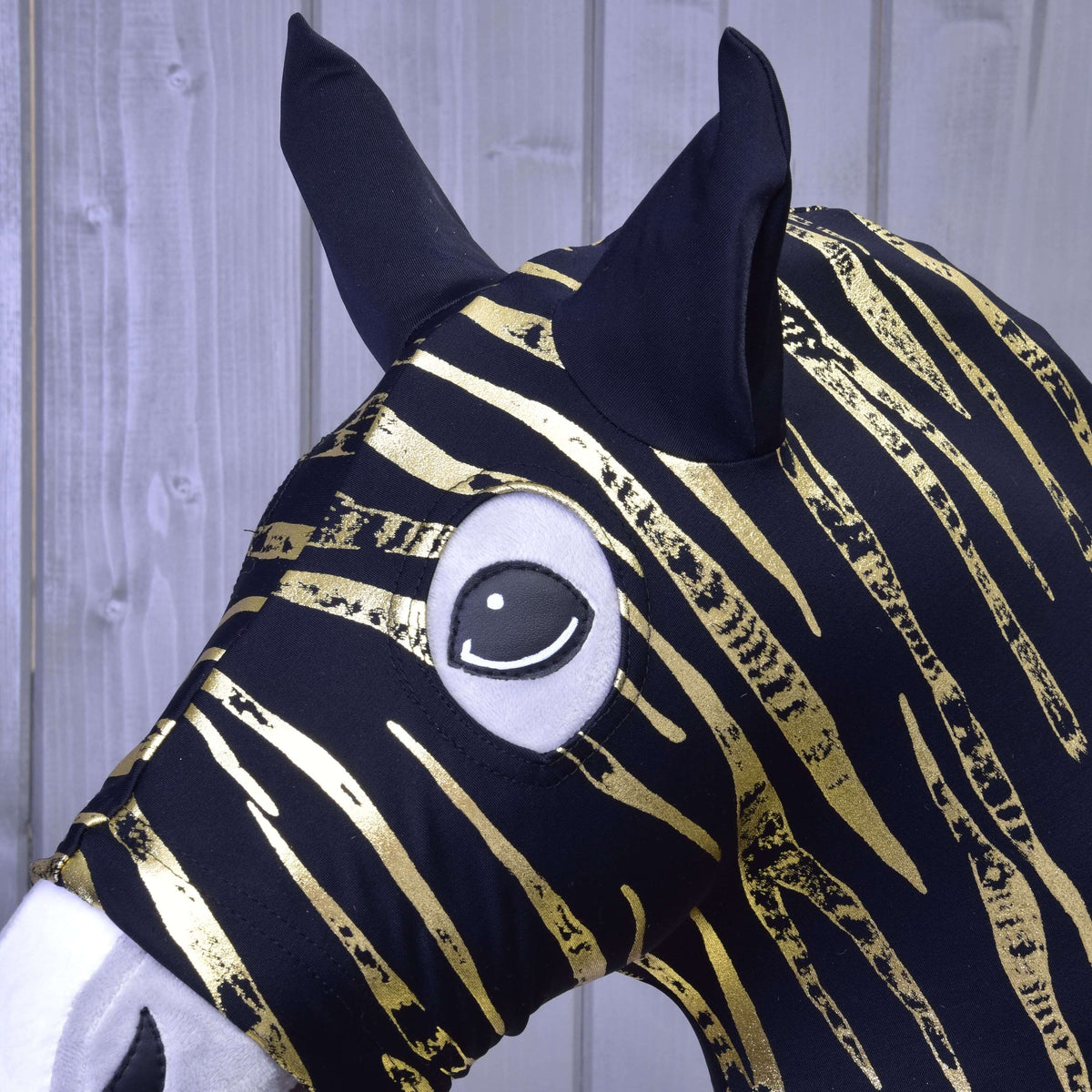 Bližnji posnetek zlatih zebrastih črt, črnih ušesnih delov in okrogle odprtine za oko zaščitne obleke iz materiala Lycra na Hobby Horse konju