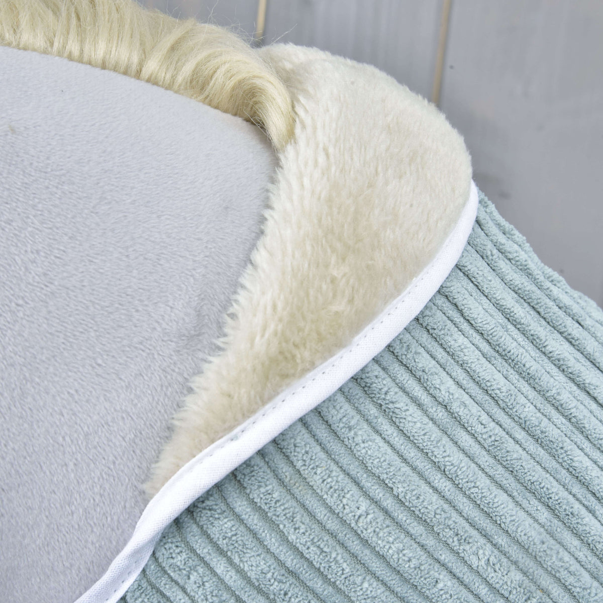 Detail of the cream fleece collar edged in white piping against the wide sage green corduroy of the blanket