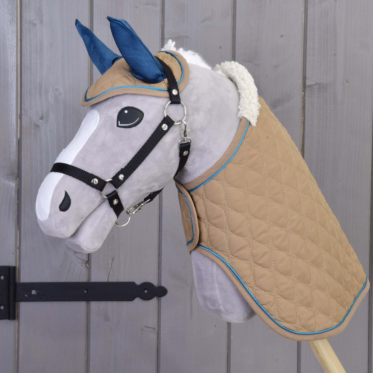 Siv plišast Hobby Horse konj nosi bež prešit komplet Almond Star s temno modrimi ušesnimi deli, ovratnikom iz umetnega ovčjega krzna in črno oglavko
