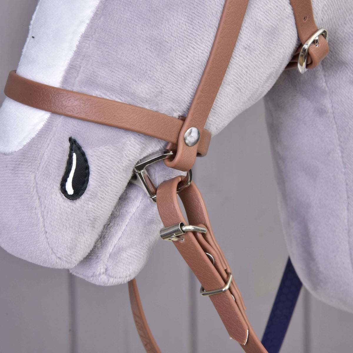 Close-up of the tan leatherette noseband with silver buckles and rein clip on the muzzle of a grey Hobby Horse
