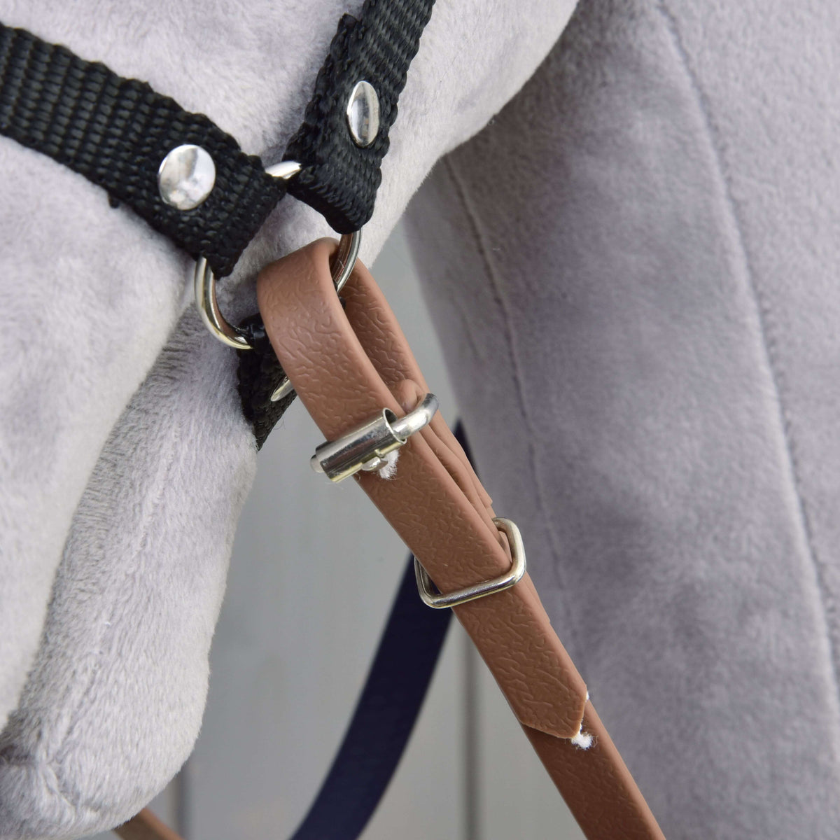 Close-up of the brown rein end with buckle and keeper fastened to the black halter ring of a grey Hobby Horse