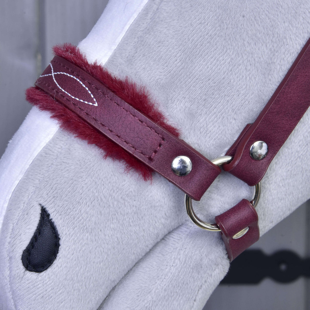 Bližnji posnetek bordo nosnika s krzneno obrobo, belimi okrasnimi šivi in srebrnim obročkom na sivem Hobby Horse konju