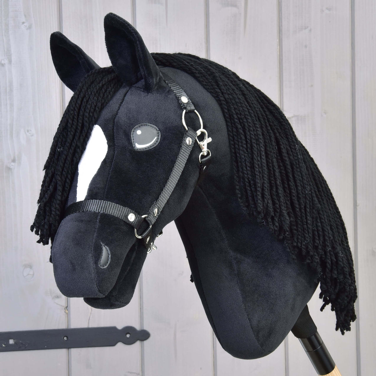 Hobby Horse konj Cloony, rahlo obrnjen proti fotoaparatu, z belo zvezdo, sivim našitim očesom in črno oglavko iz traku