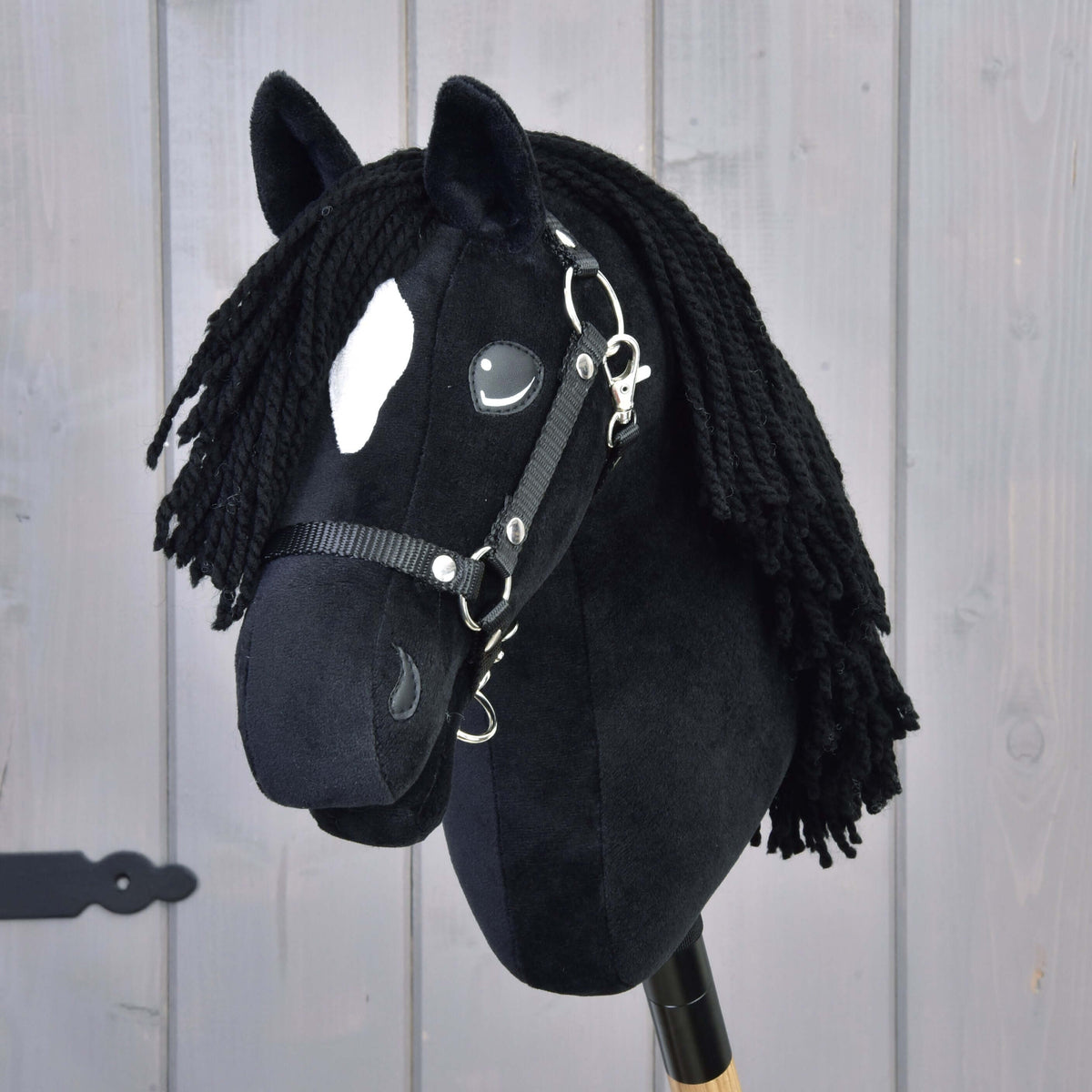 Hobby Horse konj Cloony od spredaj s črnim čopom iz preje, belo zvezdo in črno oglavko pred svetlo leseno steno
