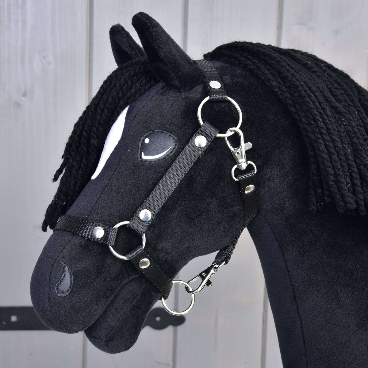 Bližnji posnetek črne oglavke na Hobby Horse konju Cloony s srebrnimi obročki, zakovicami in karabini na črnem plišu