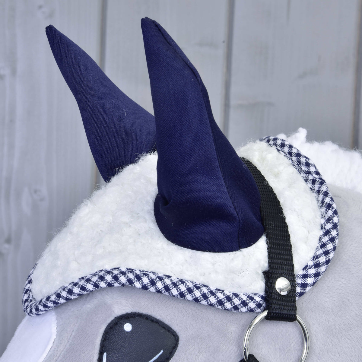Close-up of the white sherpa ear bonnet with navy ears and gingham edge on a grey Hobby Horse with a black halter