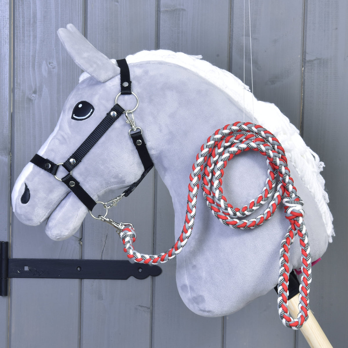 Siv Hobby Horse konj z belo grivo in črno oglavko s pripetim rdeče-belim pletenim povodcem, zvitim čez vrat