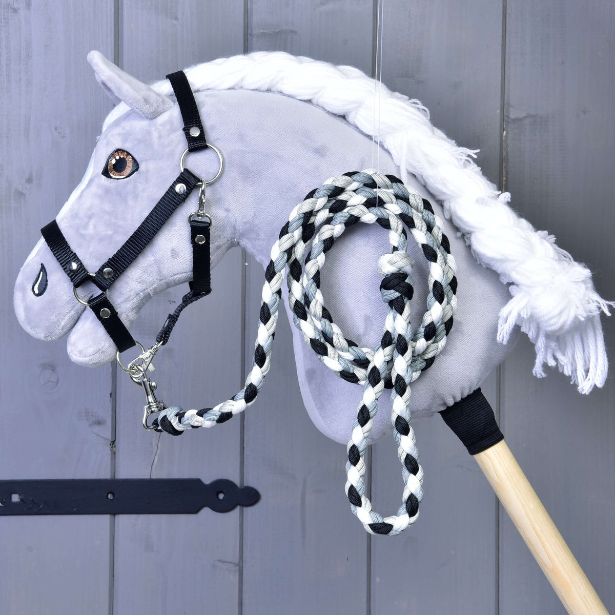 Siv plišast Hobby Horse konj s črno oglavko, na katero je pripet zvit črno-belo-siv pleten povodec