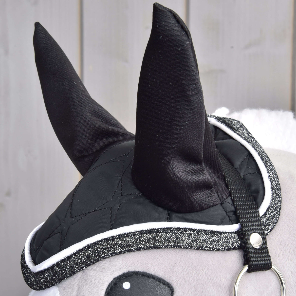 Close-up of the Set Thermo Black Queen ear bonnet with black ears and glittery trim on a grey Hobby Horse