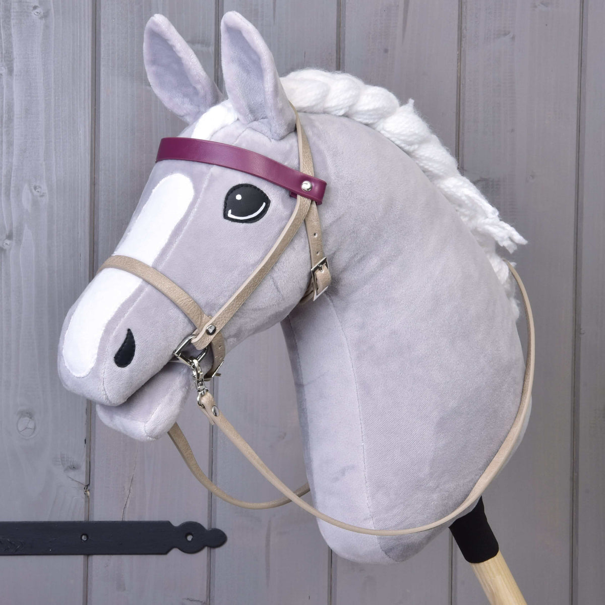 Grey Hobby Horse wearing the beige leatherette bridle with bordeaux browband and long beige reins, three-quarter view