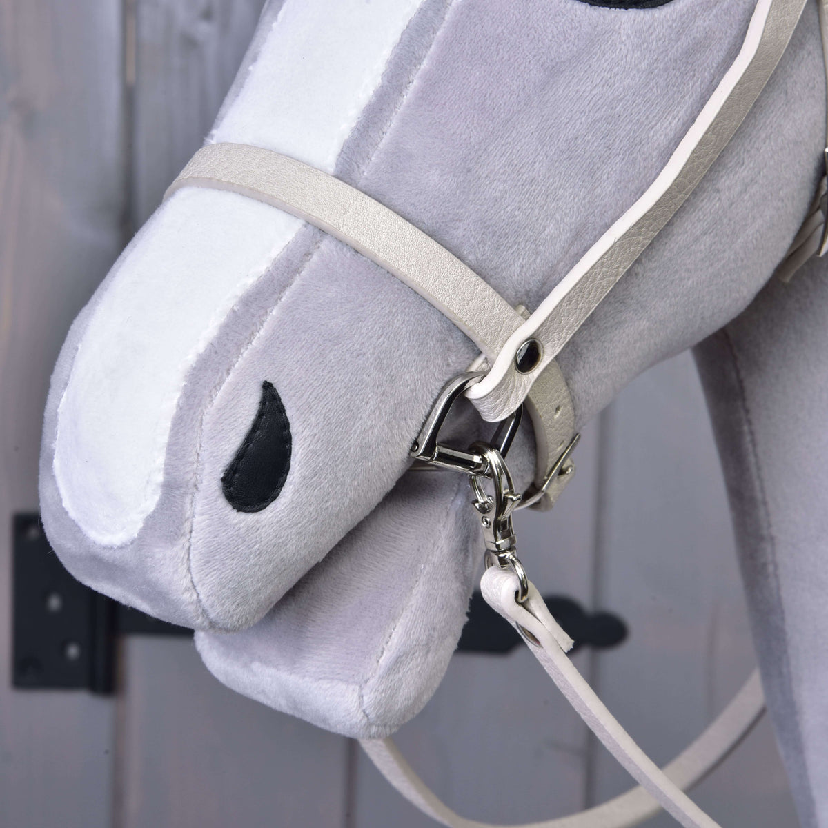 Bližnji posnetek smetanastega nosnika in karabina z vajetmi na gobcu sivega Hobby Horse konja