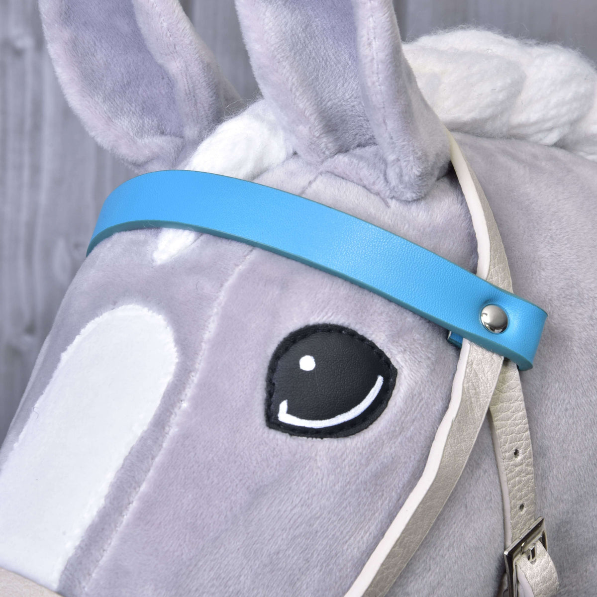 Bližnji posnetek turkizno modrega čelnika iz umetnega usnja s srebrno zakovico ob očesu sivega Hobby Horse konja