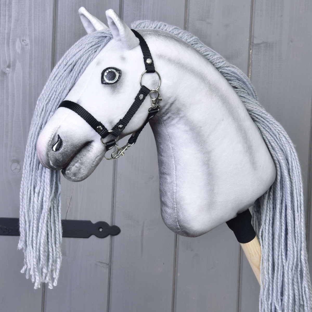 Hobby Horse samorog Silver brez roga s črno oglavko in leseno palico pred sivimi deskami