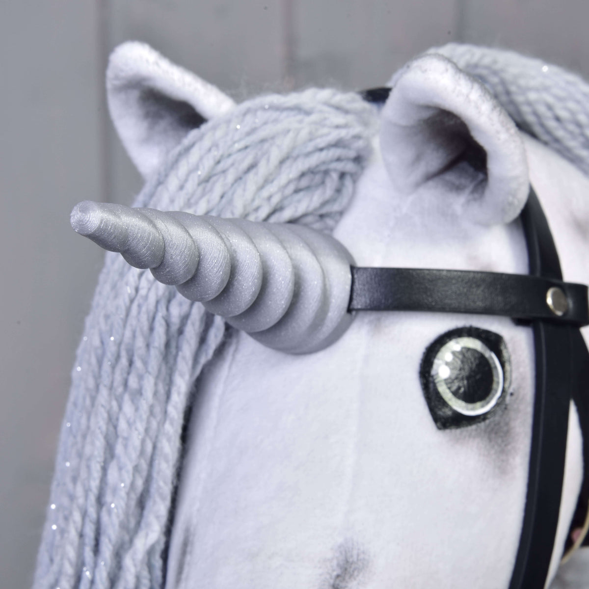 Bližnji posnetek srebrnega spiralnega roga Hobby Horse samoroga Silver, pritrjenega na črno uzdo med ušesi