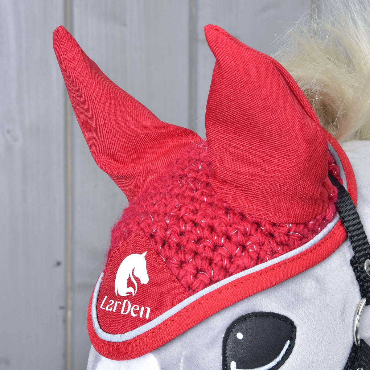 Bližnji posnetek kvačkanih naušnikov Red Sport na sivem Hobby Horse konju: rdeča ušesa iz blaga, bleščeče kvačkanje in logotip LarDen