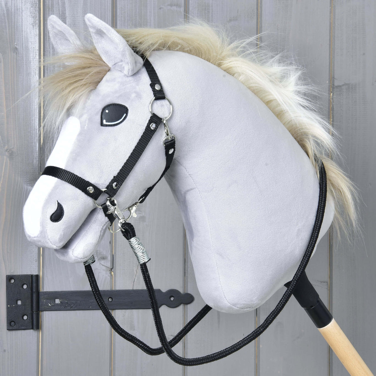 Siv Hobby Horse konj z blond grivo in črno oglavko, črne pletene vajeti so pripete na obeh straneh in ohlapno visijo