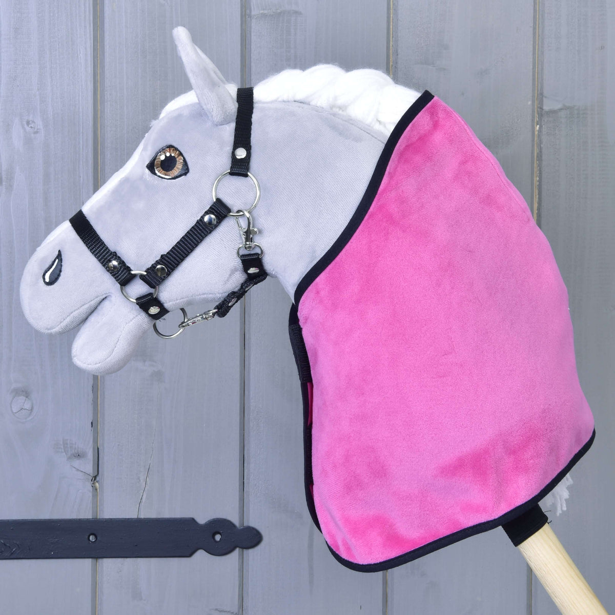 Siv Hobby Horse konj v črni oglavki nosi samo živo roza žametasto pregrinjalo s črno obrobo