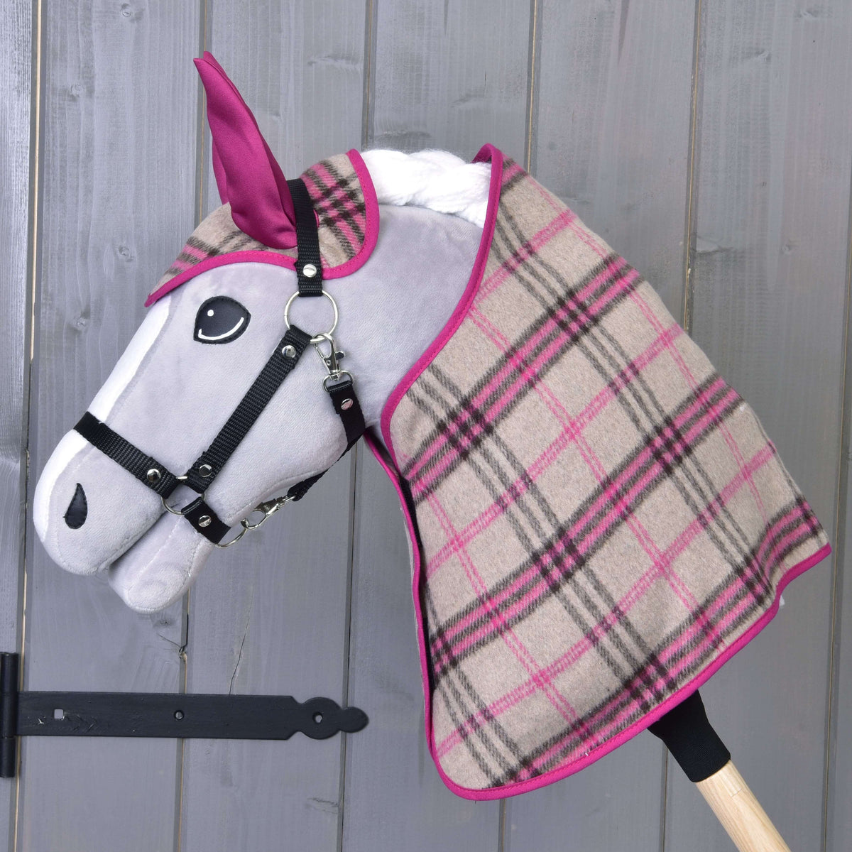 Siv Hobby Horse konj v črni oglavki nosi bež-roza karirasto pregrinjalo in naušnike z roza ušesnimi deli