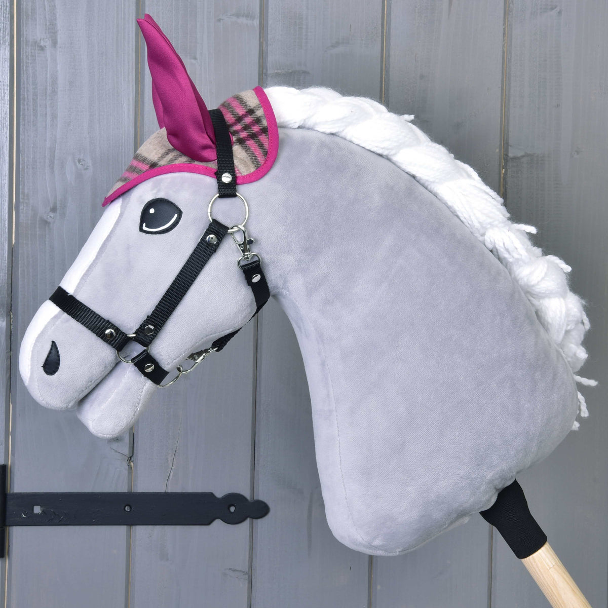 Siv Hobby Horse konj v črni oglavki nosi samo kariraste naušnike z roza ušesnimi deli in roza obrobo