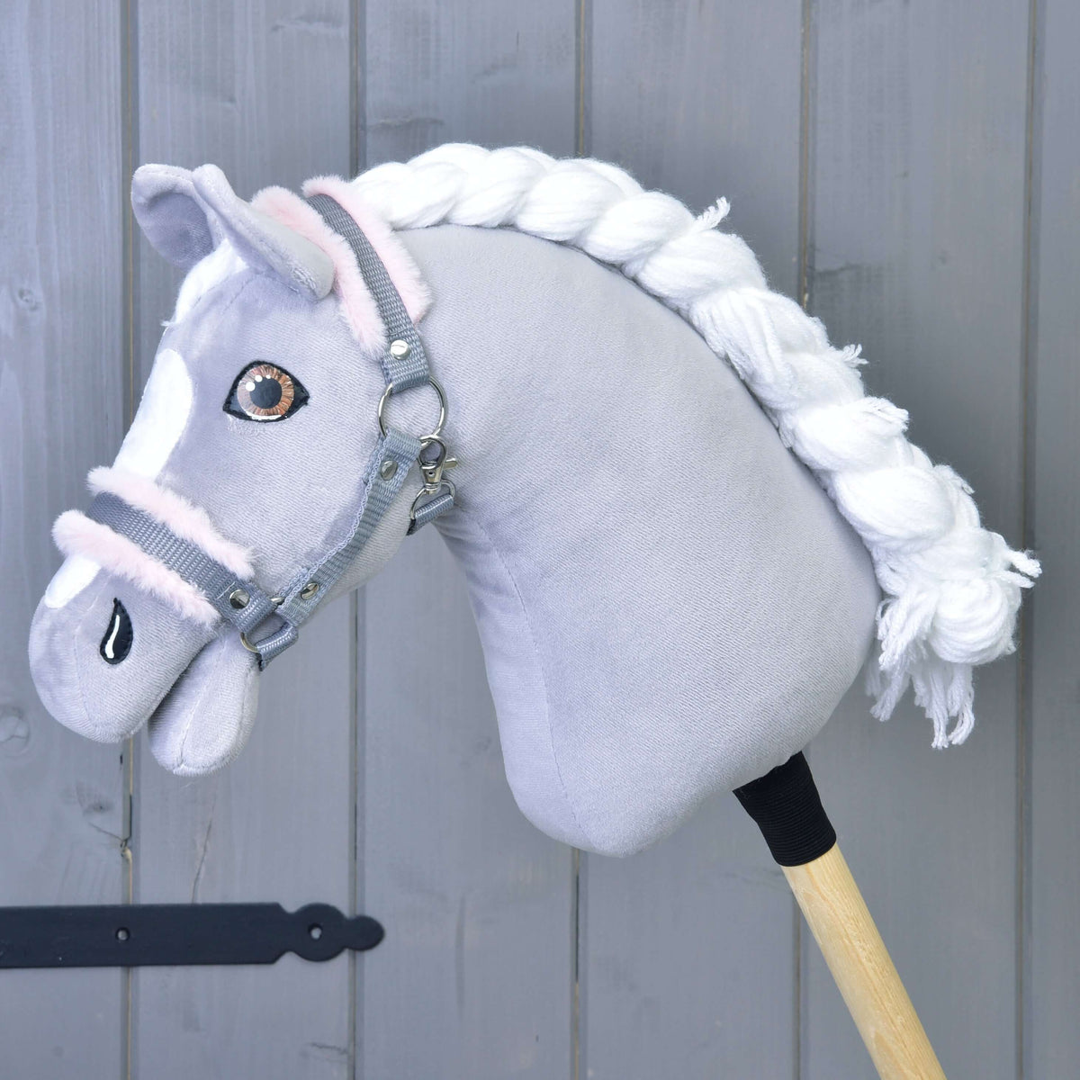 Siv plišast Hobby Horse konj s spleteno belo grivo in rjavimi očmi nosi sivo oglavko s svetlo roza krznom