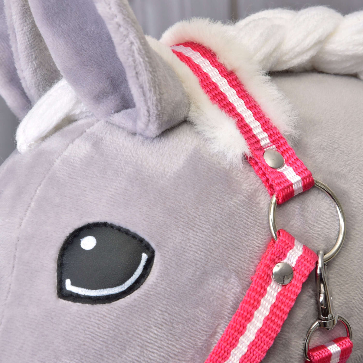 Close-up of the red striped crownpiece with white fur beside the ear of a grey Hobby Horse, with ring and snap hook