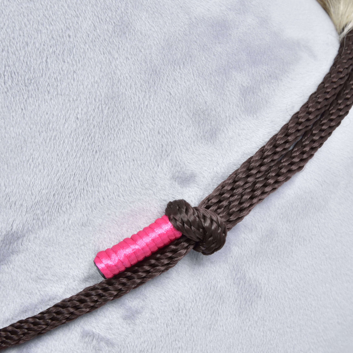 Brown rope knot with a bright pink wrapped end from Rope set Noir Cocoa, lying on a grey plush neck