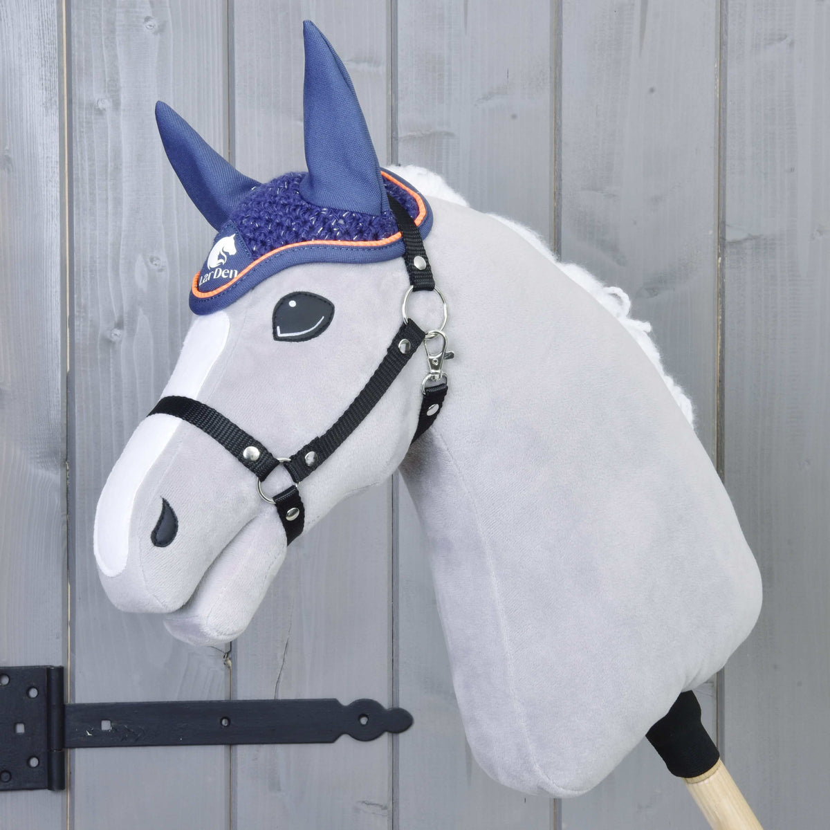 Siv plišast Hobby Horse konj z belo liso in črno oglavko nosi temno modre kvačkane naušnike z oranžnim paspulom