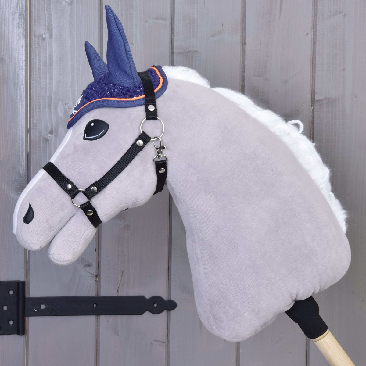 Pogled od strani na sivega Hobby Horse konja z belo grivo in črno oglavko, ki nosi kvačkane naušnike Blue Sport