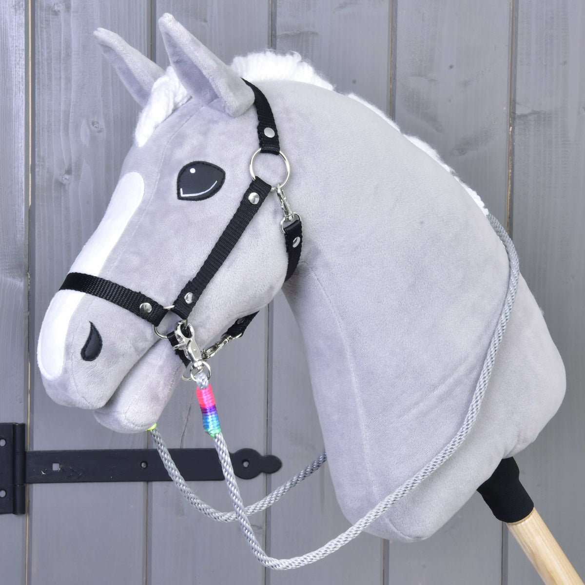 Siv plišast Hobby Horse konj s črno oglavko in sivimi vrvičnimi vajetmi Manhattan z mavričnim ovojem ob karabinu