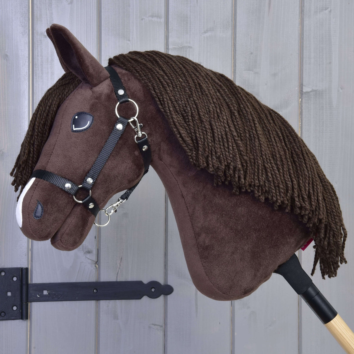 Pogled od strani na temno rjavega Hobby Horse konja z dolgo rjavo grivo iz preje in črno najlonsko oglavko s karabinom