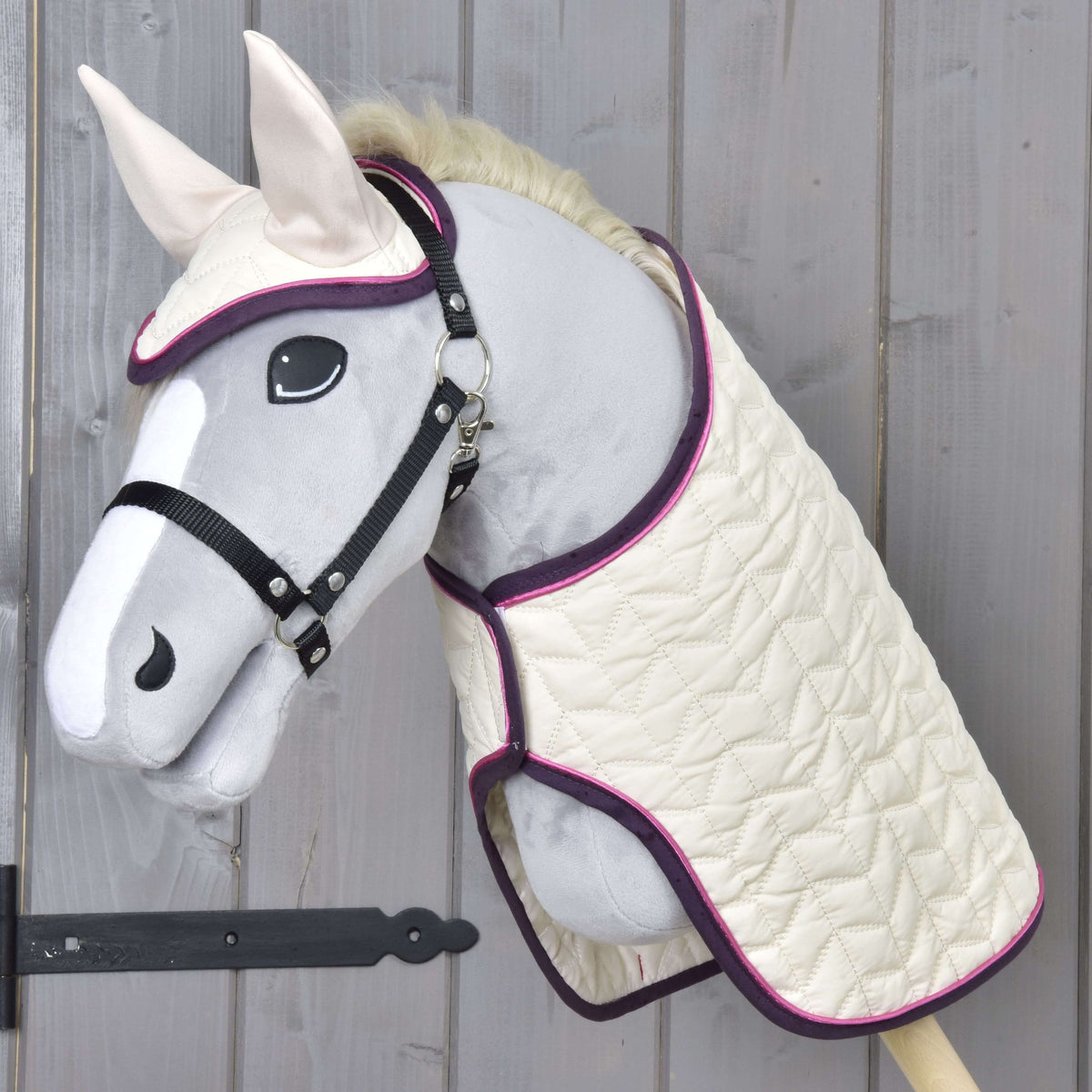 Light grey Hobby Horse in a black halter wearing the Set Supreme Crema, a cream quilted blanket and matching ear bonnet