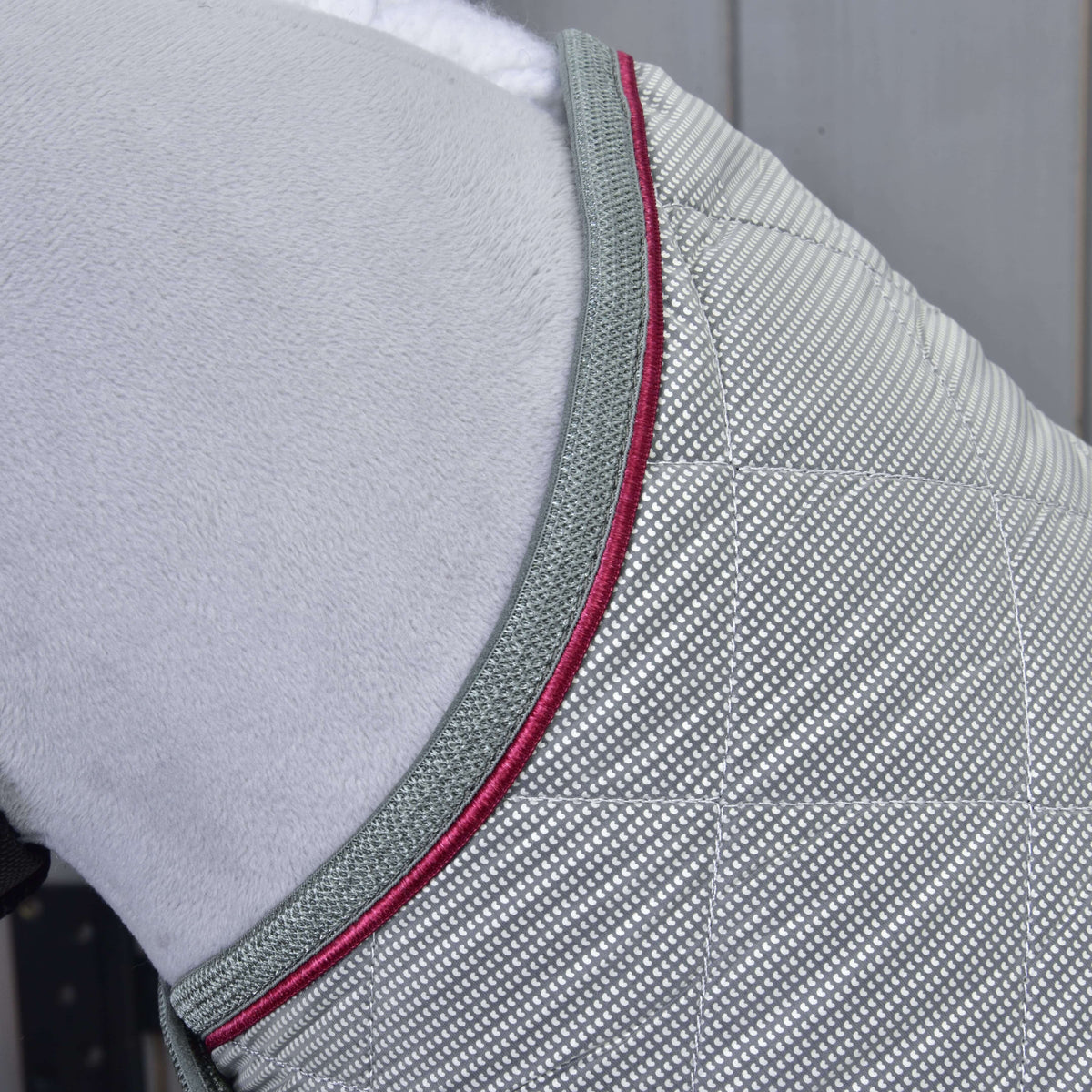 Detail of the quilted silver blanket at the neck, edged with grey binding and a raspberry red piping
