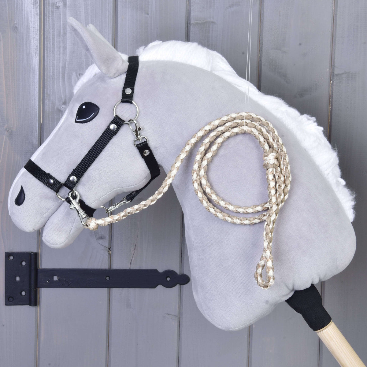 Pleten povodec v kremni in bež barvi, pripet na črno oglavko sivega Hobby Horse konja ob sivi leseni steni