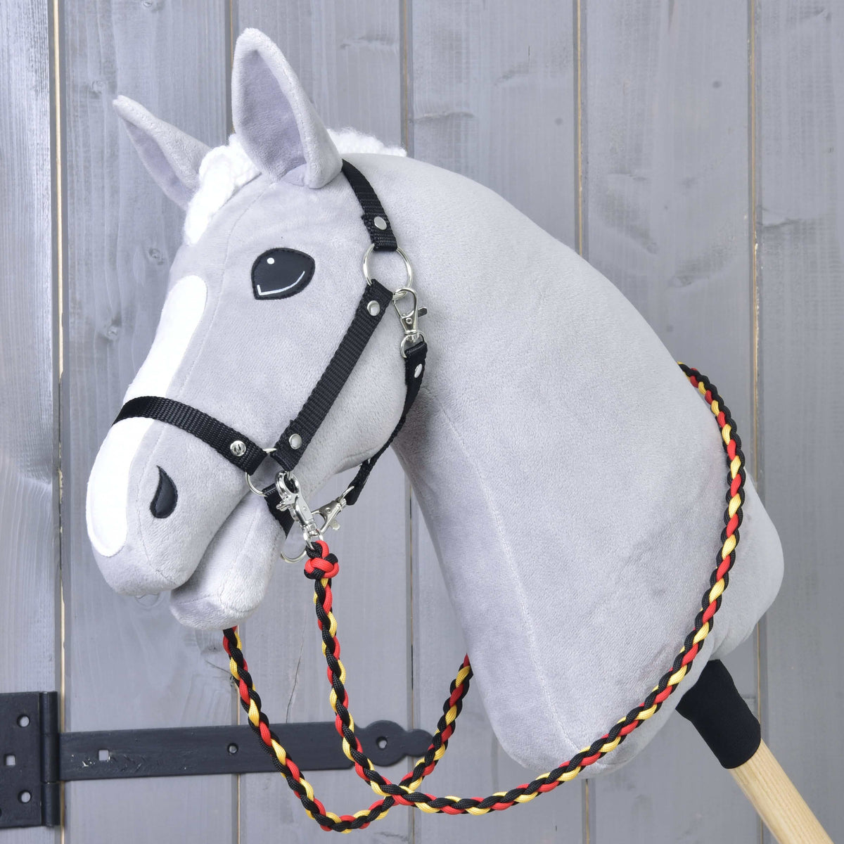 Svetlo siv Hobby Horse konj s črno oglavko in pletenimi črno-rdeče-rumenimi vajetmi Flag okoli vratu