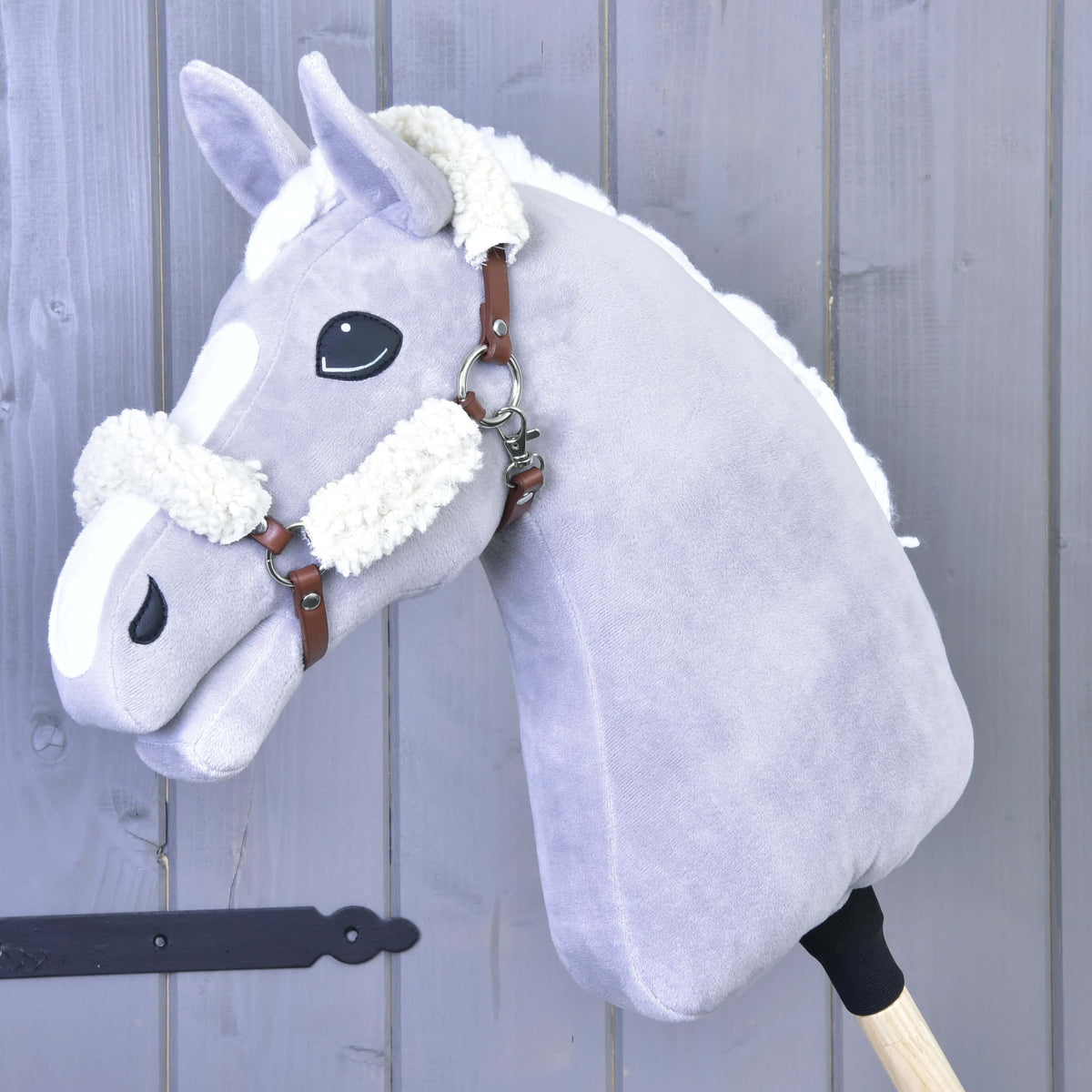 Svetlo siv Hobby Horse konj z belo grivo nosi rjavo oglavko iz umetnega usnja s smetanastim krznom na zatilnem jermenu in nosniku
